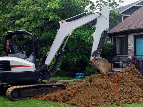 Excavator digging in a hole and creating a large dirt pile in a residential front yard.