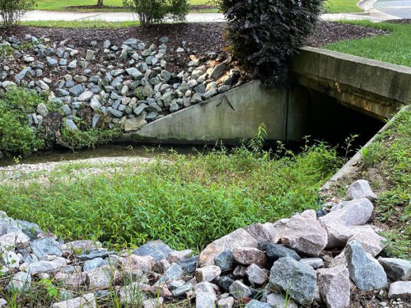 Stone stormwater culvert lined with rocks in a suburban neighborhood.