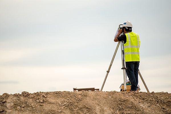 A surveryor in a yellow vest working on a dirt hill.
