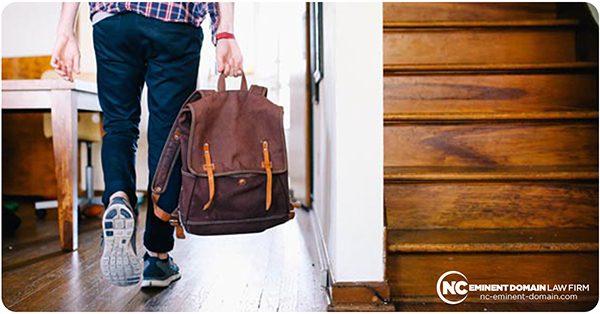 Man with back turned getting ready to walk out of home with backpack in his hand.