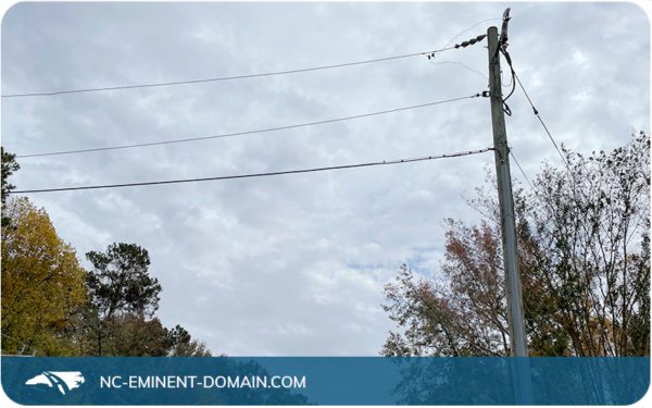 Power lines against a cloudy sky near a forested area.