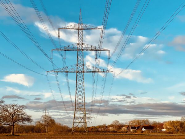 Power lines and tower against a blue sky crossing over a field with houses.