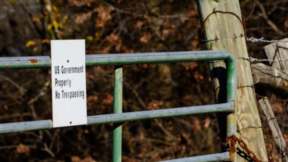 Barbed wire fence with a green gate that has a sign saying, 'US Government property. No trespassing."