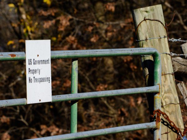 Barbed wire fence with a green gate that has a sign saying, 'US Government property. No trespassing."