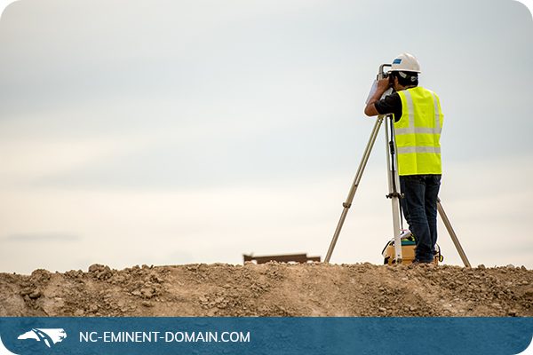 A surveyor in a hi vis vest working on a dirt hill.