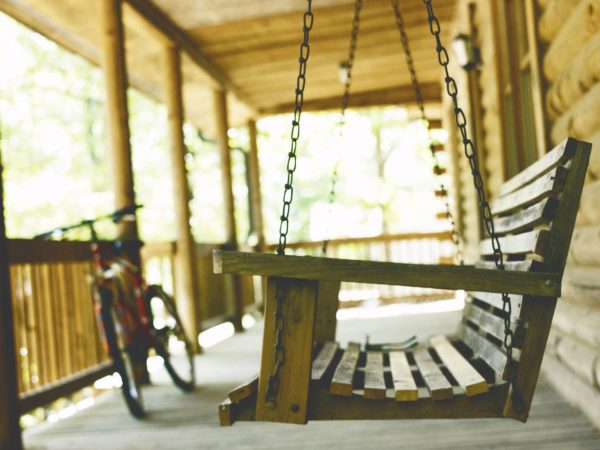 Porch swing with red bike leaning on porch in the background.