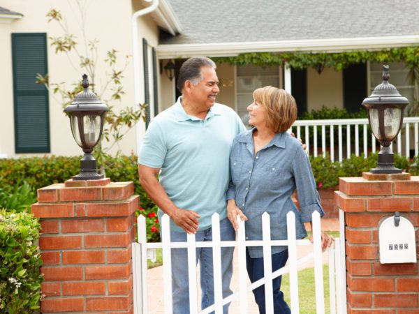 A couple looking at each other and smiling at the entrance gate of a house.