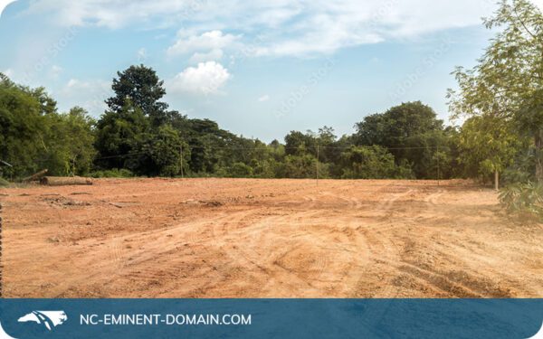 A vacant bulldozed dirt lot lined with trees.